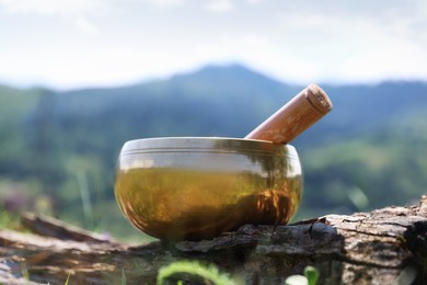 Photo of Tibetan singing bowl with mallet on piece of wood outdoors, closeup
