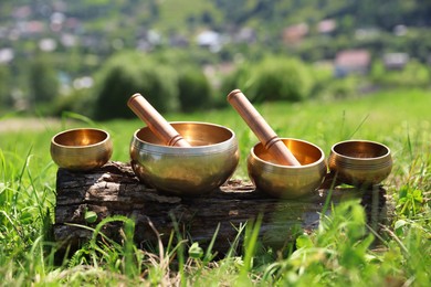 Photo of Tibetan singing bowls with mallets on piece of wood outdoors
