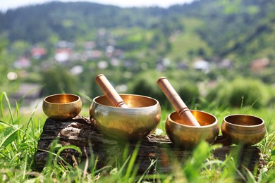 Photo of Tibetan singing bowls with mallets on piece of wood outdoors