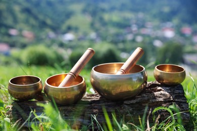 Photo of Tibetan singing bowls with mallets on piece of wood outdoors, closeup