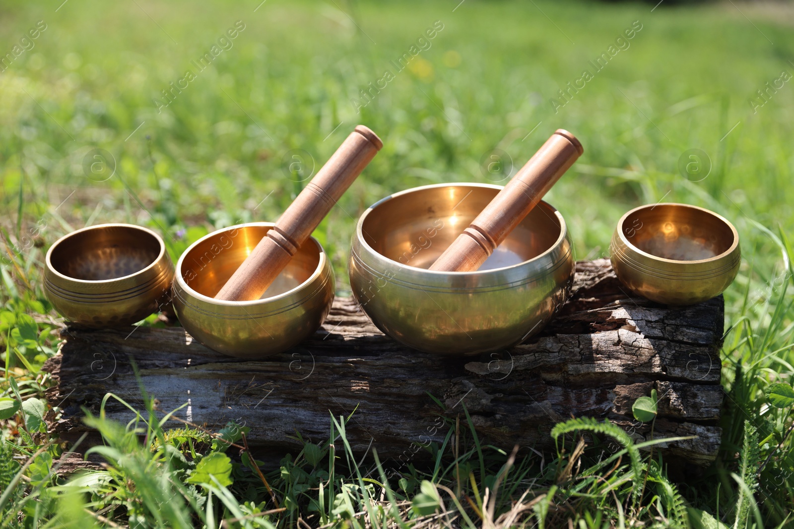 Photo of Tibetan singing bowls with mallets on piece of wood outdoors