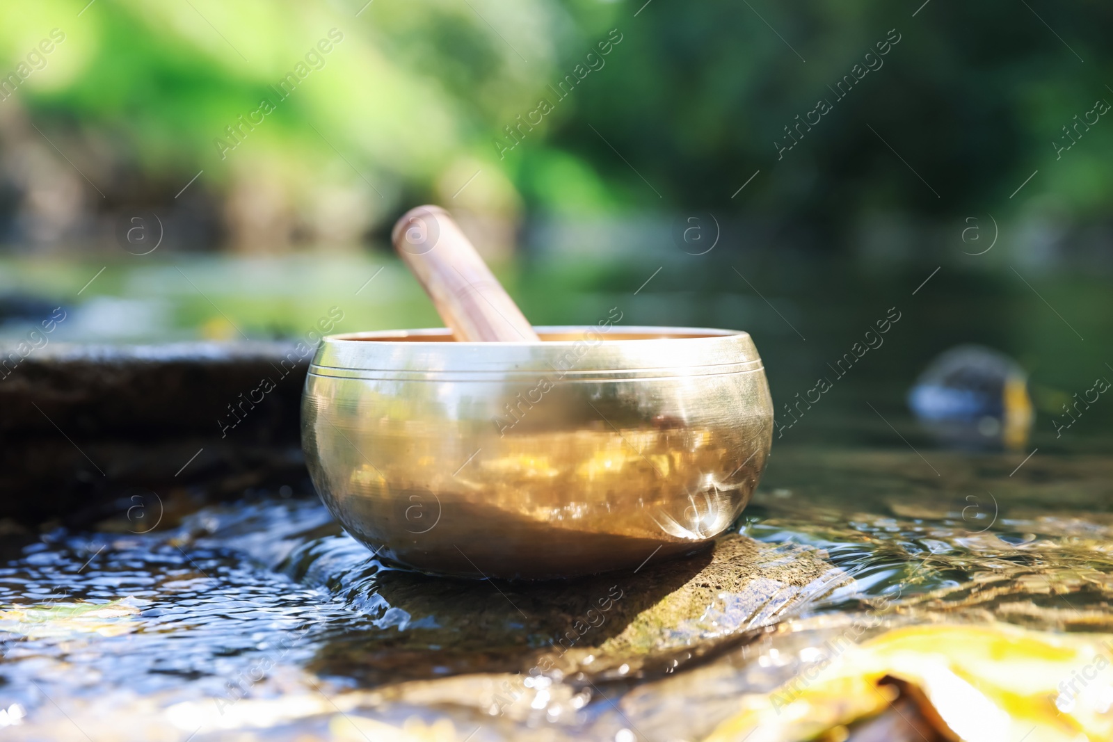 Photo of Tibetan singing bowl with mallet on stone near river, closeup