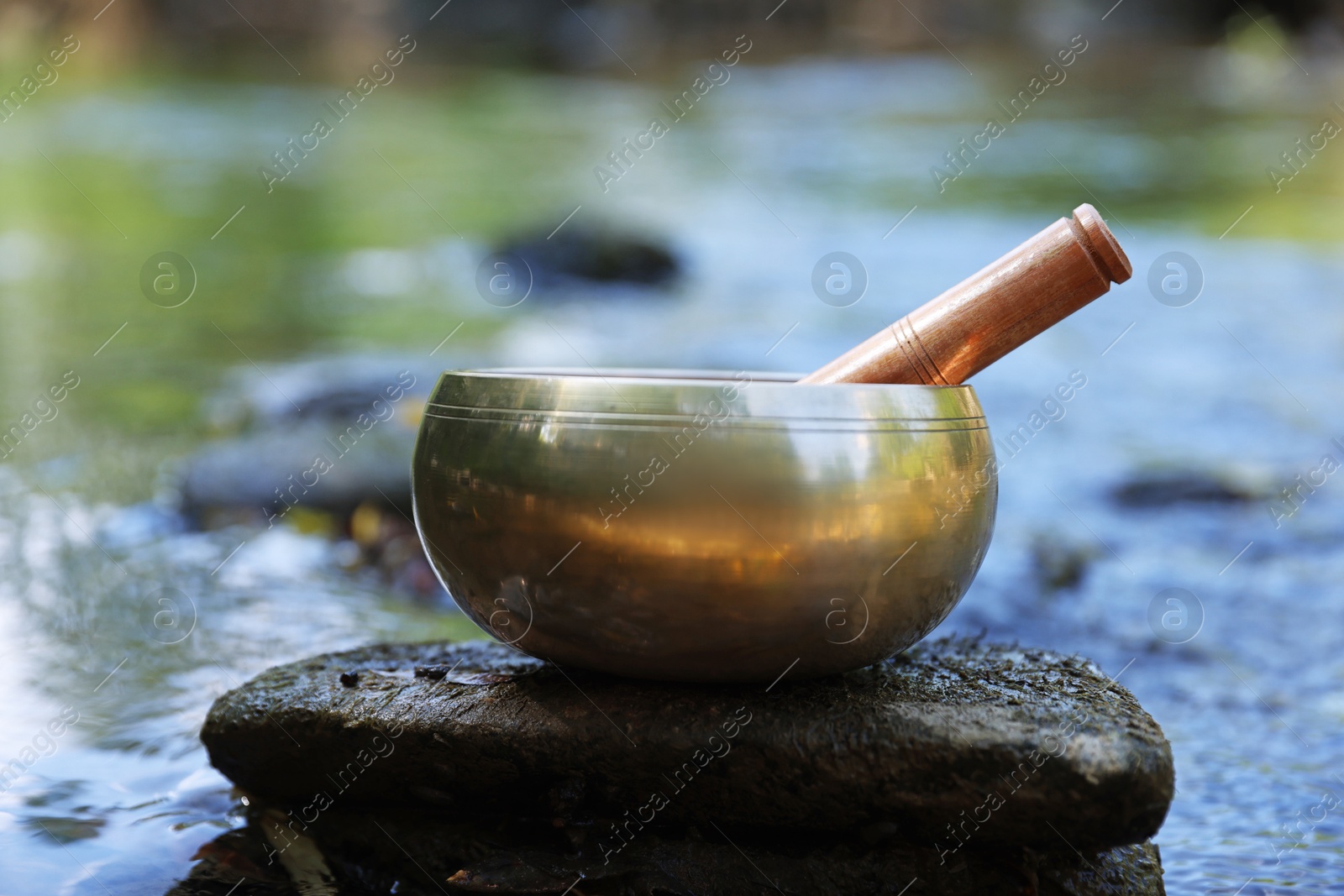 Photo of Tibetan singing bowl with mallet on stone near river, closeup