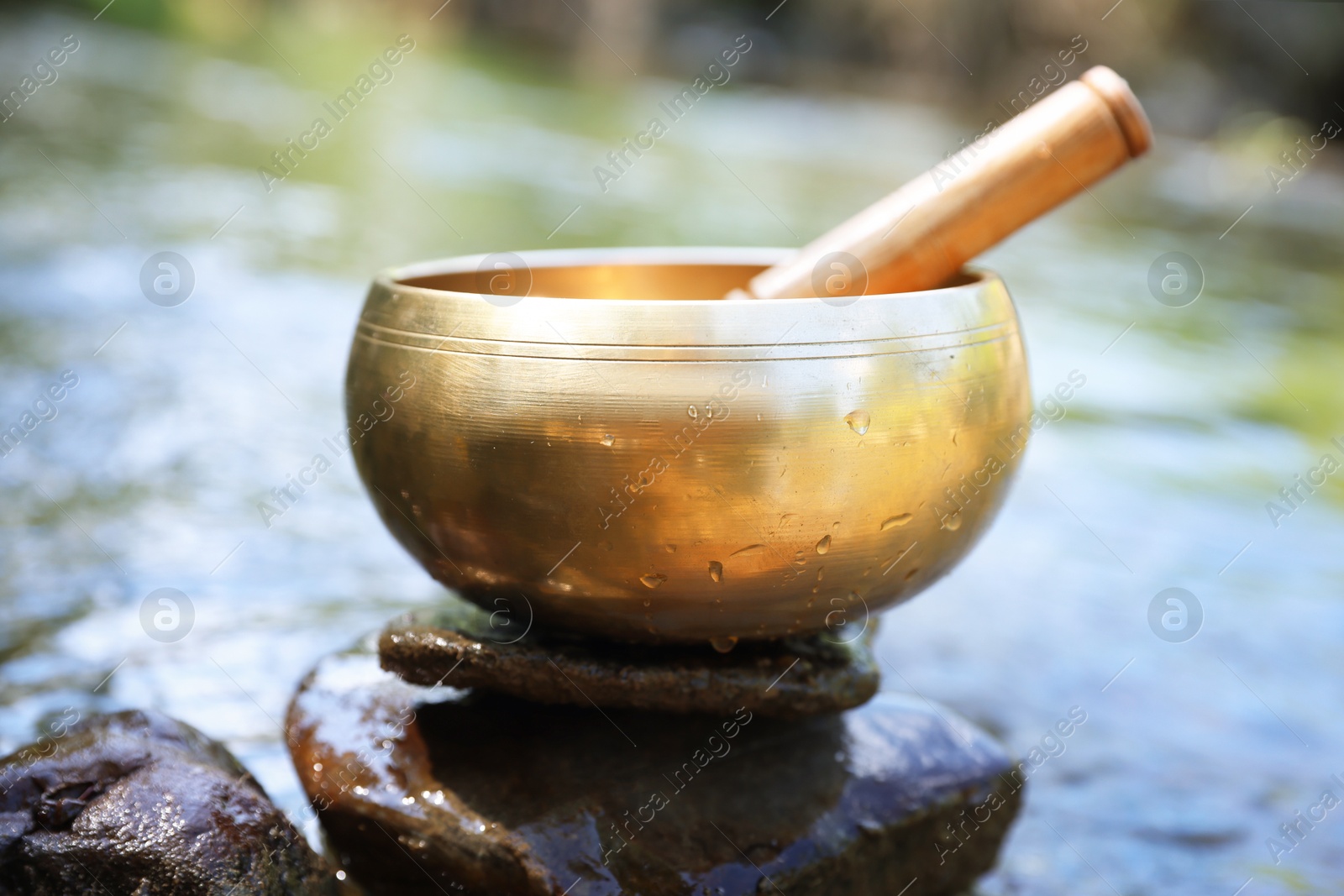 Photo of Tibetan singing bowl with mallet on stone near river, closeup