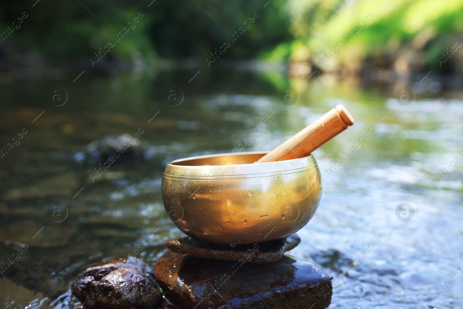 Photo of Tibetan singing bowl with mallet on stone near river