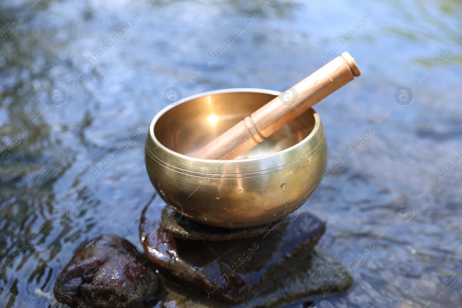 Photo of Tibetan singing bowl with mallet on stone near river, closeup