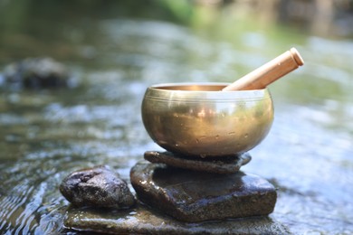 Photo of Tibetan singing bowl with mallet on stone in river, closeup