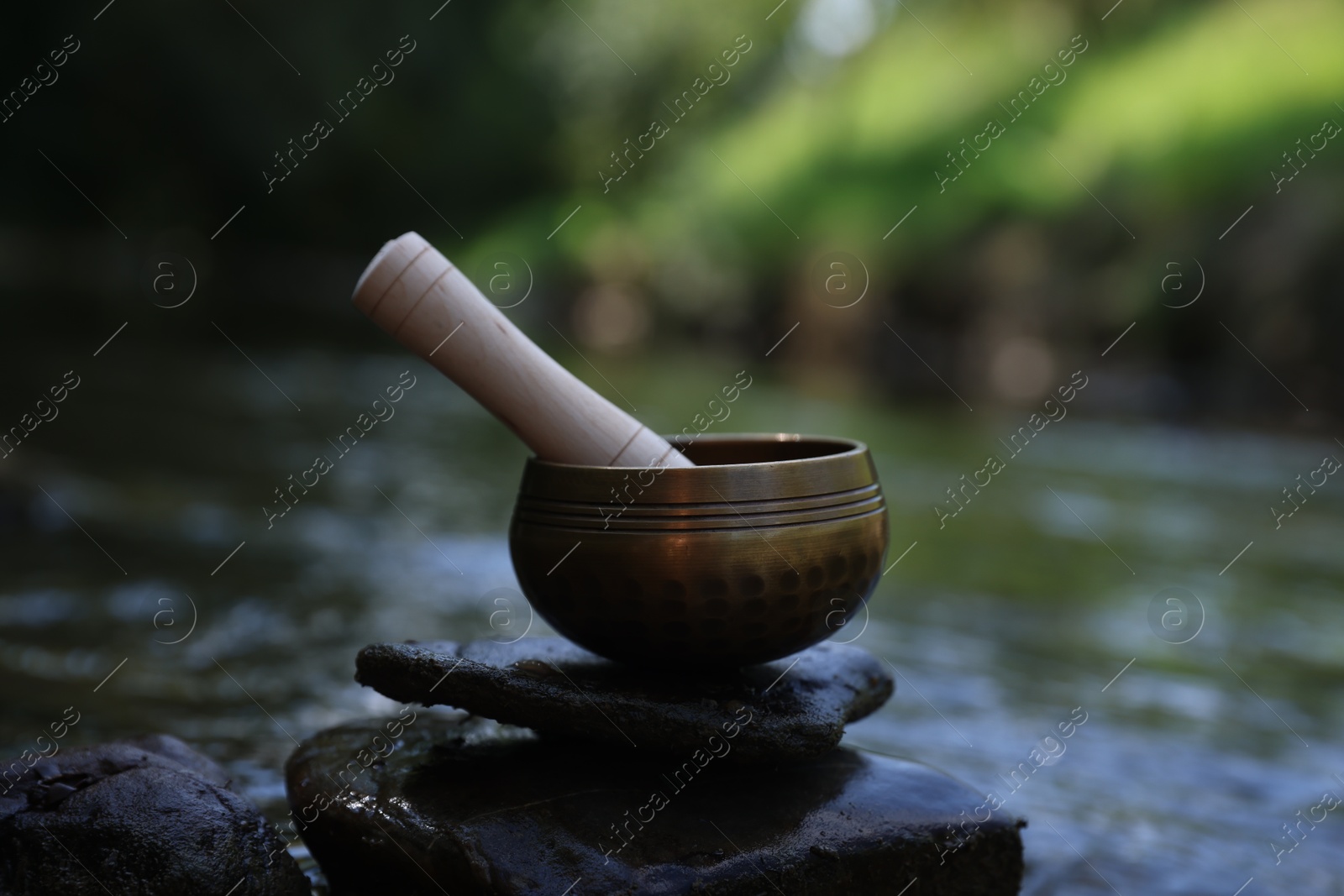 Photo of Tibetan singing bowl with mallet on stone near river