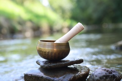 Photo of Tibetan singing bowl with mallet on stone near river
