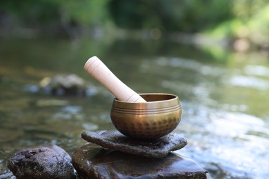 Photo of Tibetan singing bowl with mallet on stone near river