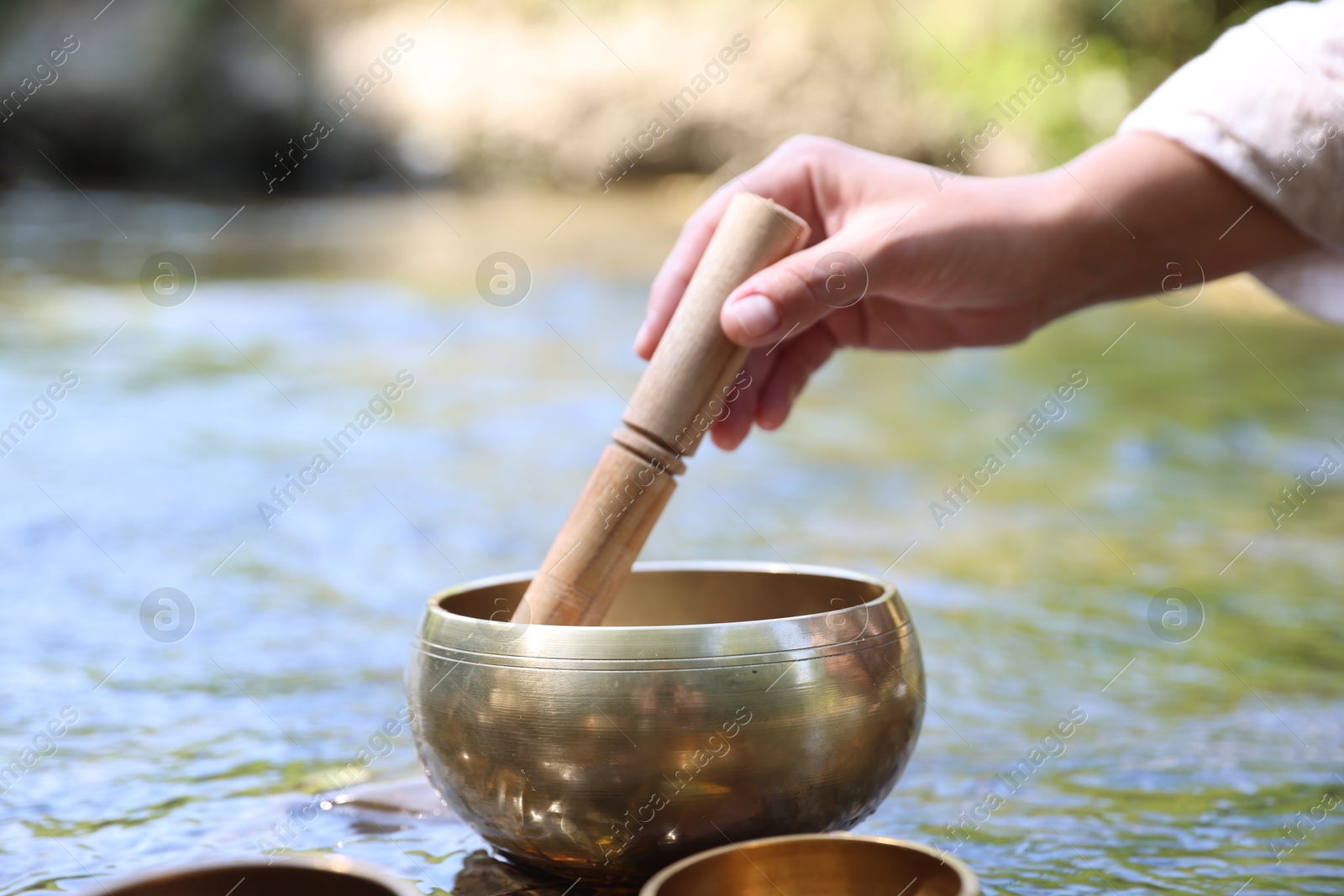 Photo of Woman with singing bowl by river, closeup