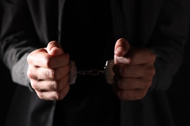Photo of Man in metal handcuffs on black background, closeup