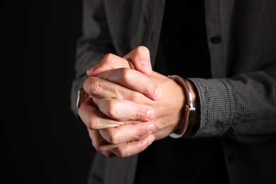 Photo of Man in metal handcuffs on black background, closeup