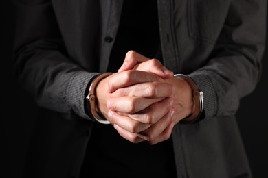 Photo of Man in metal handcuffs on black background, closeup