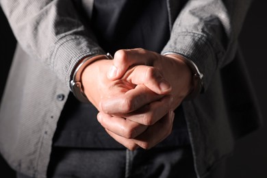 Photo of Man in metal handcuffs on black background, closeup
