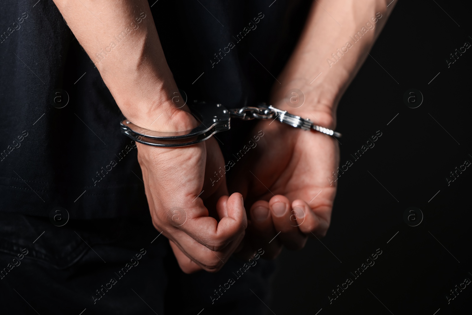 Photo of Man in metal handcuffs on black background, closeup