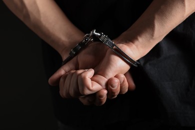 Photo of Man in metal handcuffs on black background, closeup