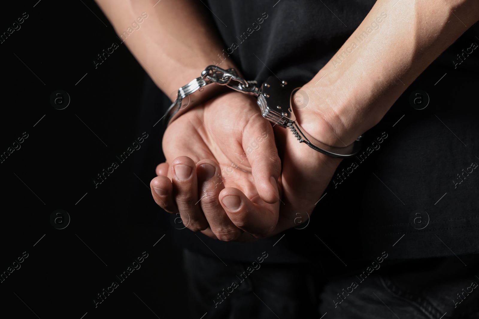 Photo of Man in metal handcuffs on black background, closeup