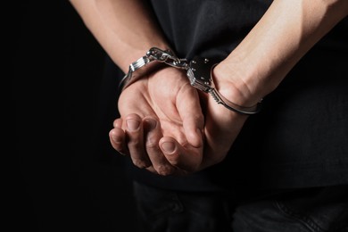 Photo of Man in metal handcuffs on black background, closeup