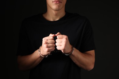 Photo of Man in metal handcuffs on black background, closeup