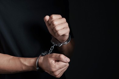 Photo of Man in metal handcuffs on black background, closeup. Space for text
