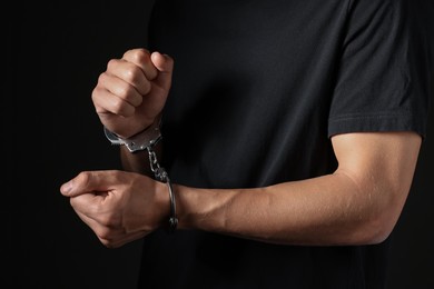 Photo of Man in metal handcuffs on black background, closeup