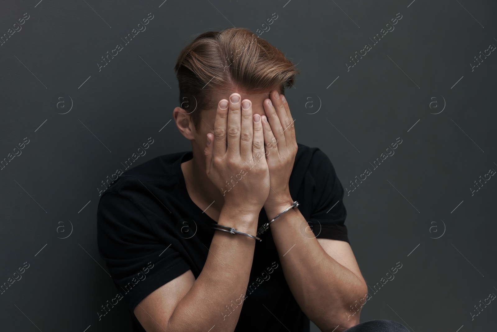 Man in metal handcuffs covering face with hands near grey wall Photo of Man in metal handcuffs covering face with hands near grey wall