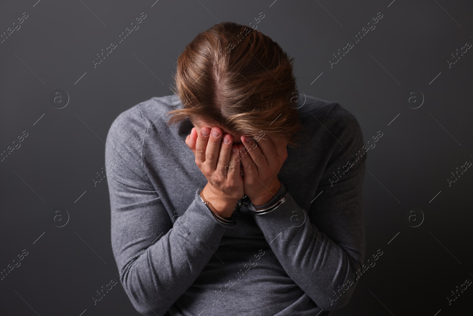 Man in metal handcuffs covering face with hands near grey wall Photo of Man in metal handcuffs covering face with hands near grey wall