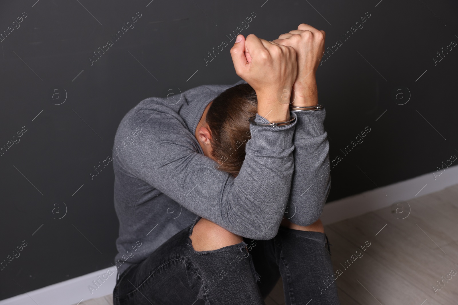 Man in metal handcuffs sitting near grey wall Photo of Man in metal handcuffs sitting near grey wall
