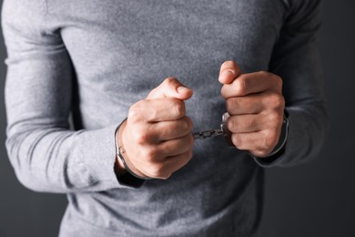 Photo of Man in metal handcuffs on grey background, closeup