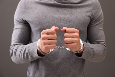 Photo of Man in metal handcuffs on grey background, closeup