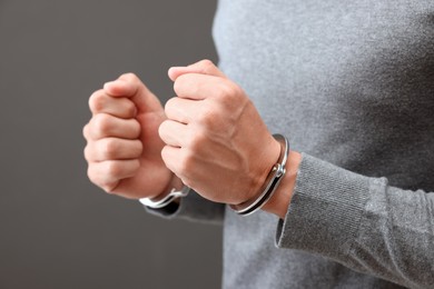 Photo of Man in metal handcuffs on grey background, closeup