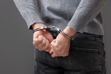Photo of Man in metal handcuffs on grey background, closeup