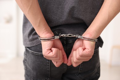 Photo of Man in metal handcuffs on blurred light background, closeup