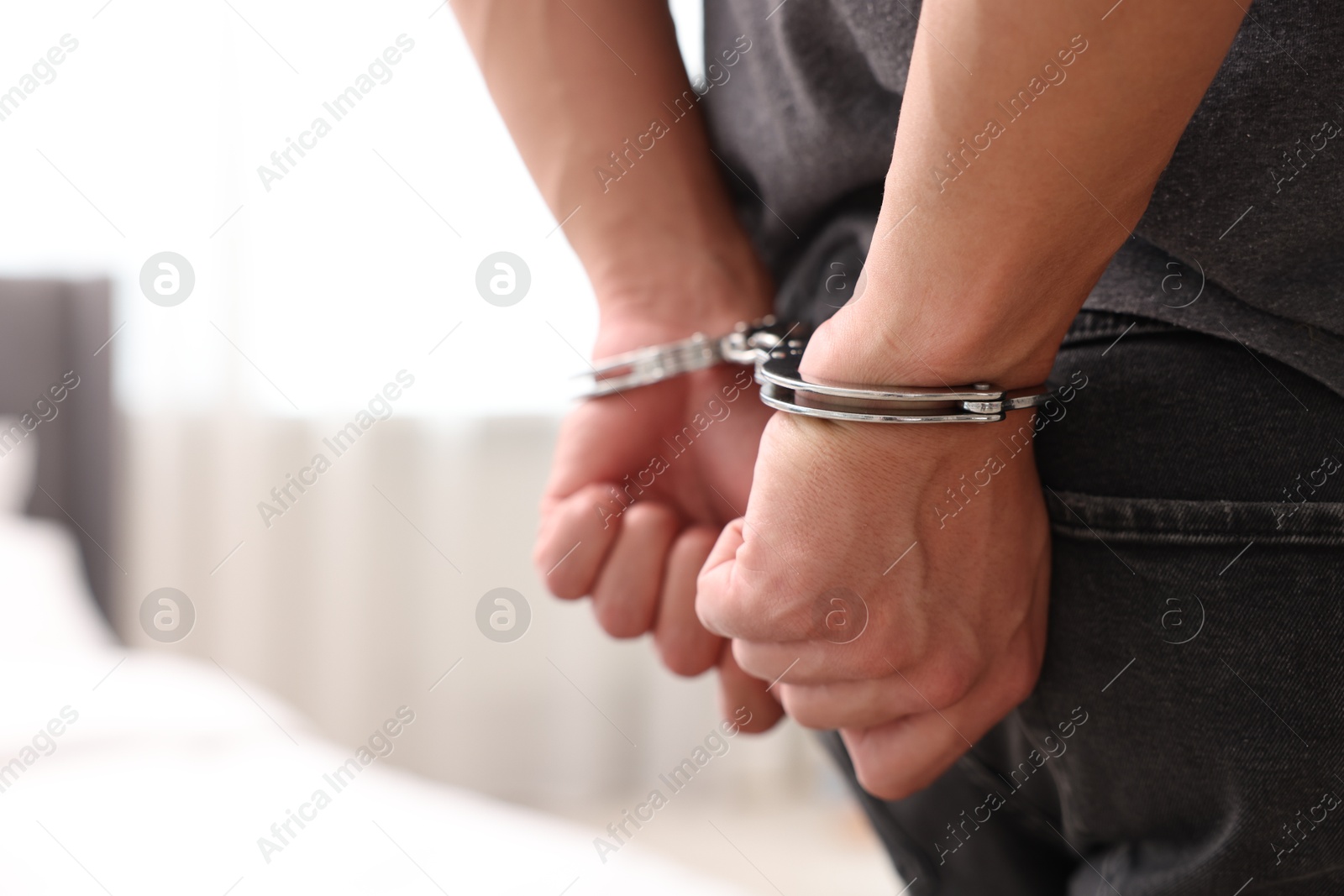 Photo of Man in metal handcuffs on blurred light background, closeup. Space for text