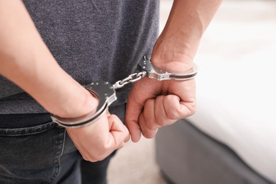 Photo of Man in metal handcuffs on blurred light background, closeup