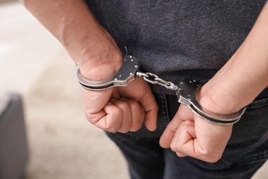 Photo of Man in metal handcuffs on blurred background, closeup