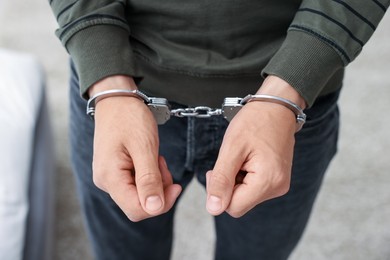 Photo of Man in metal handcuffs on blurred background, closeup