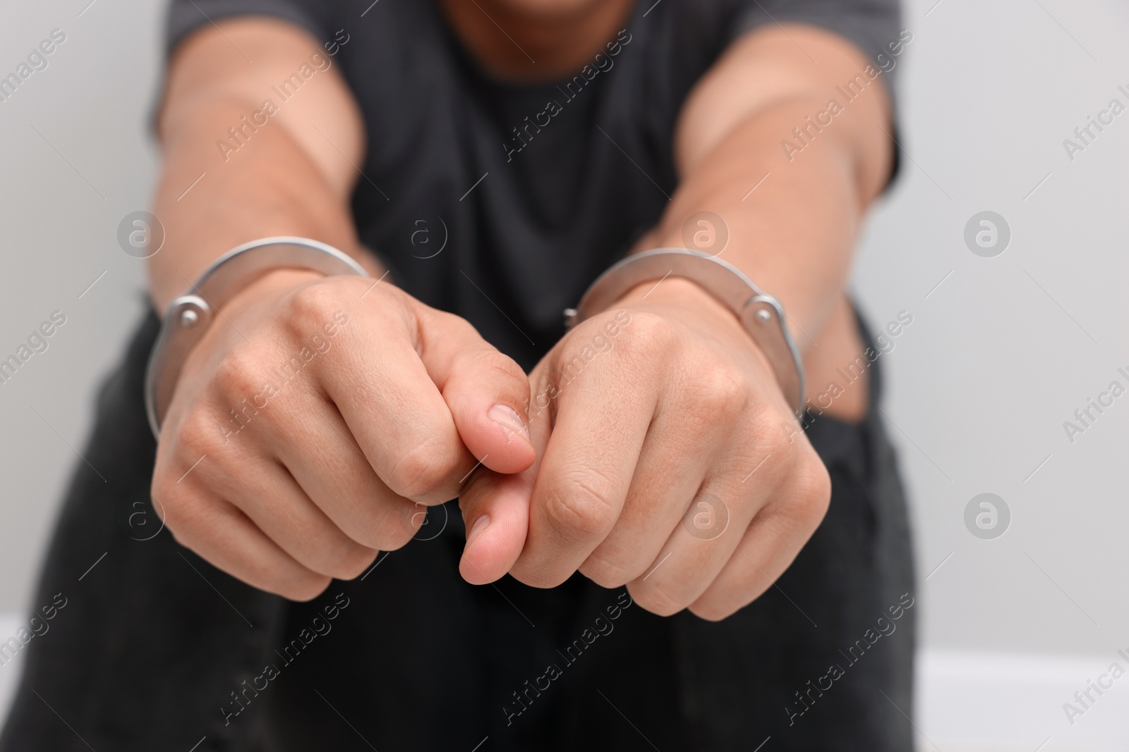 Photo of Man in metal handcuffs on light grey background, closeup
