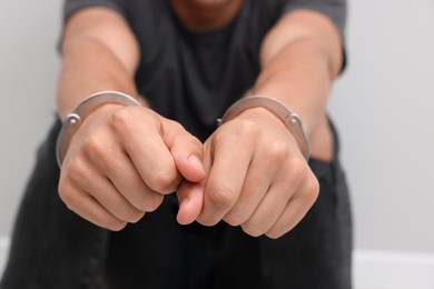 Photo of Man in metal handcuffs on light grey background, closeup