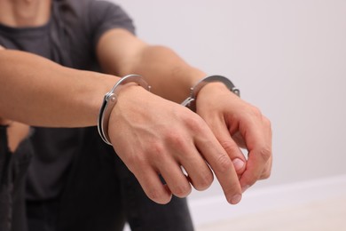 Photo of Man in metal handcuffs on light grey background, closeup