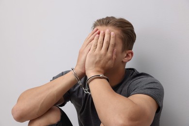 Photo of Man in metal handcuffs covering face with hands near light grey wall