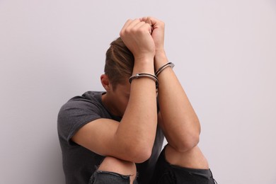 Photo of Man in metal handcuffs near light grey wall