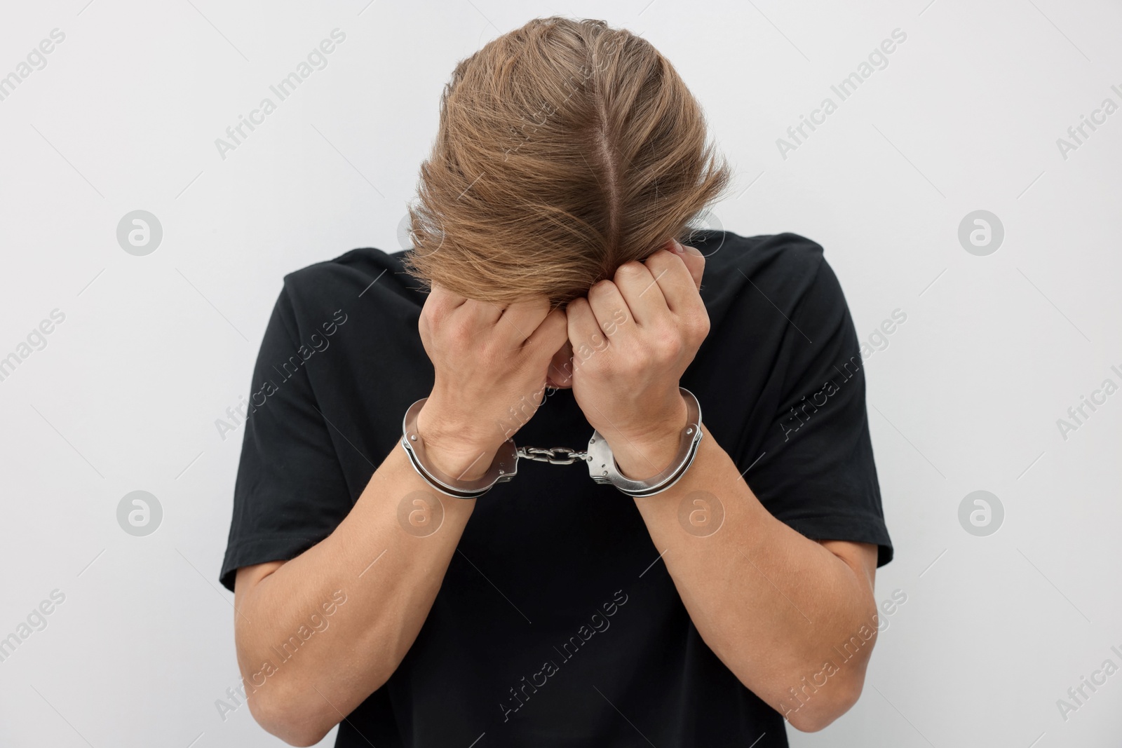 Man in metal handcuffs covering face with hands near light grey wall Photo of Man in metal handcuffs covering face with hands near light grey wall
