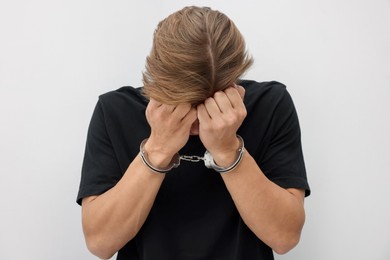 Photo of Man in metal handcuffs covering face with hands near light grey wall