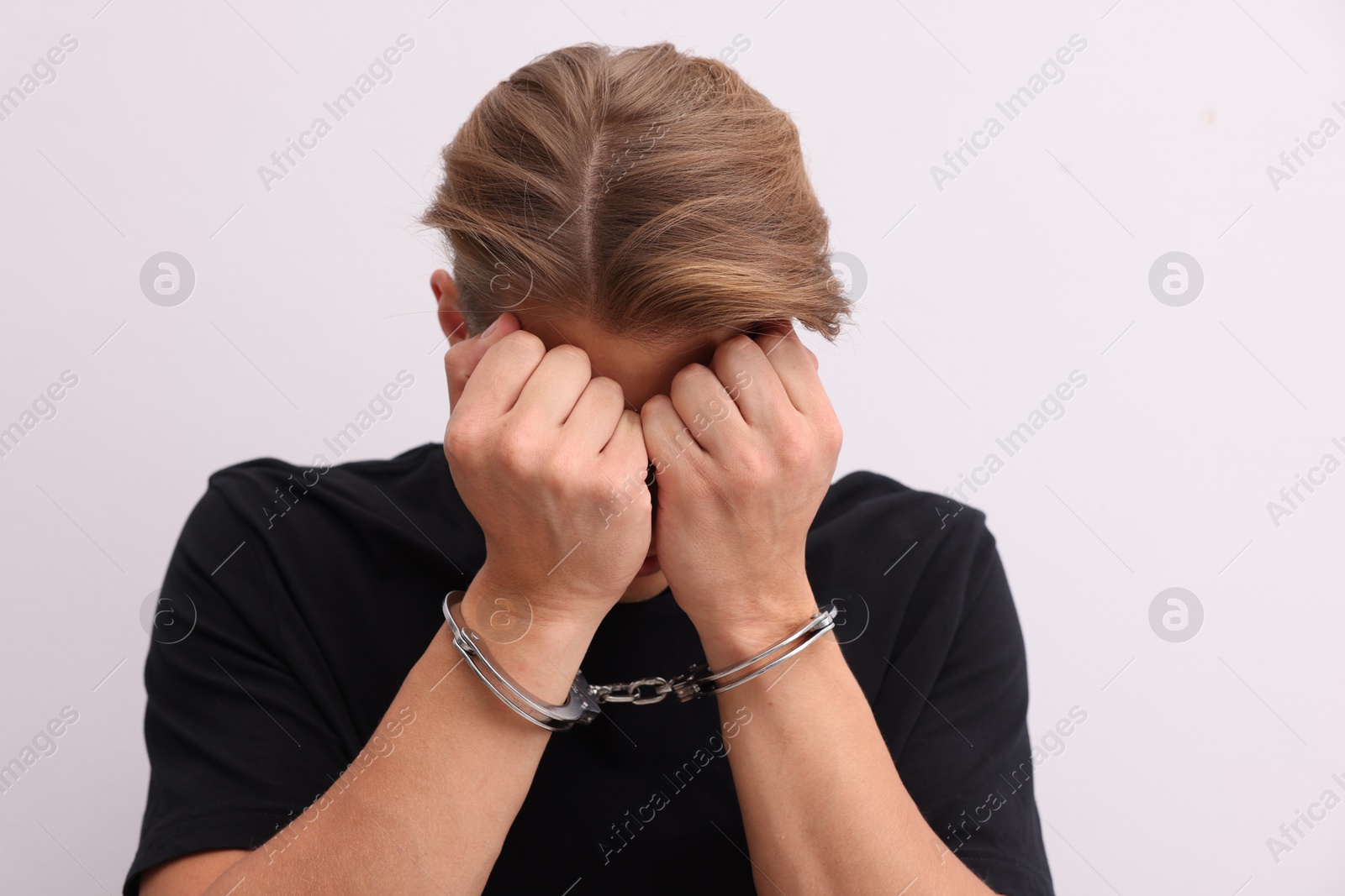Man in metal handcuffs covering face with hands near light grey wall Photo of Man in metal handcuffs covering face with hands near light grey wall