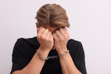 Photo of Man in metal handcuffs covering face with hands near light grey wall