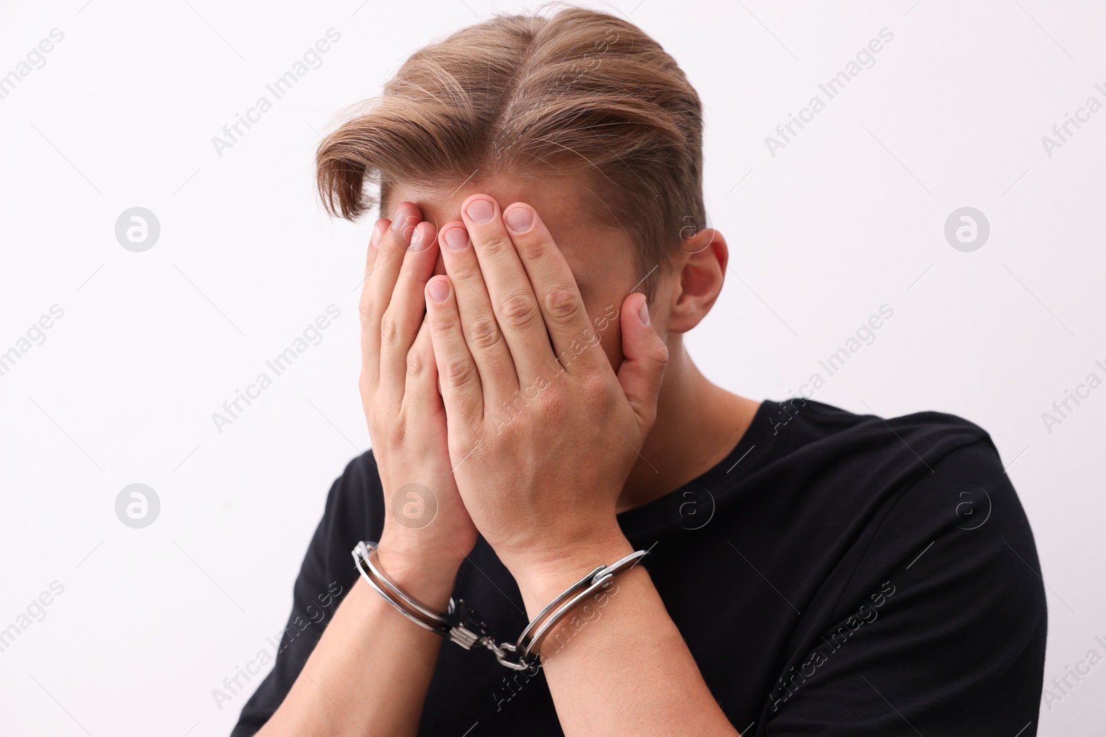 Man in metal handcuffs covering face with hands near light grey wall Photo of Man in metal handcuffs covering face with hands near light grey wall