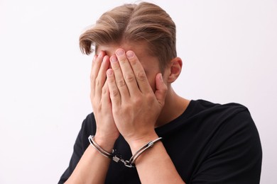 Photo of Man in metal handcuffs covering face with hands near light grey wall