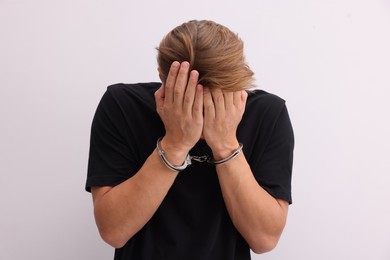 Photo of Man in metal handcuffs covering face with hands near light grey wall